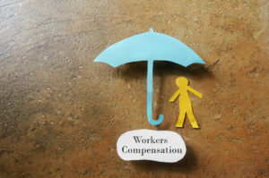 Paper man under an umbrella with Workers Compensation note underneath -- on the job injury concept